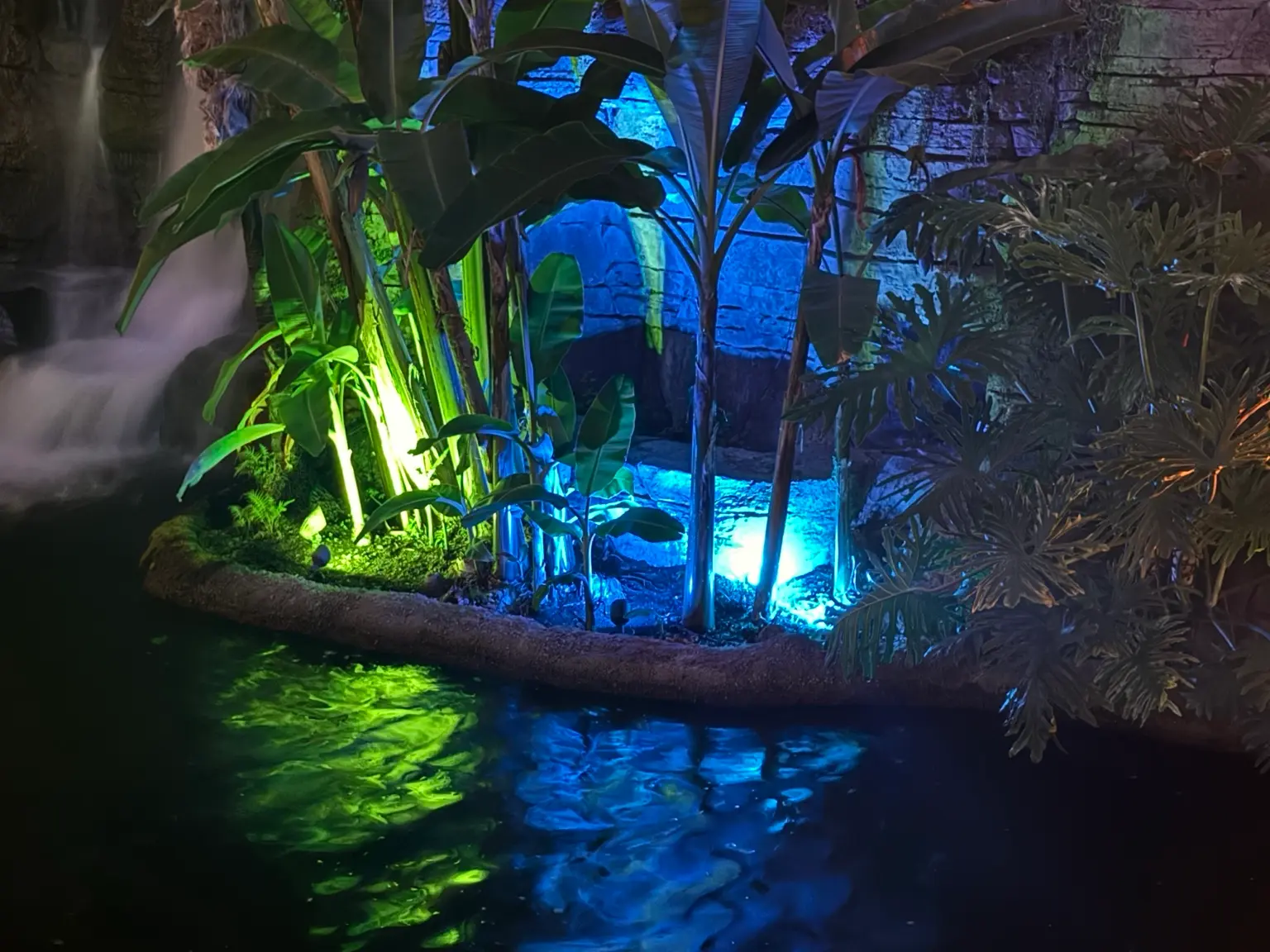 Colored landscape lighting with blue and green lights around tropical plants and water feature