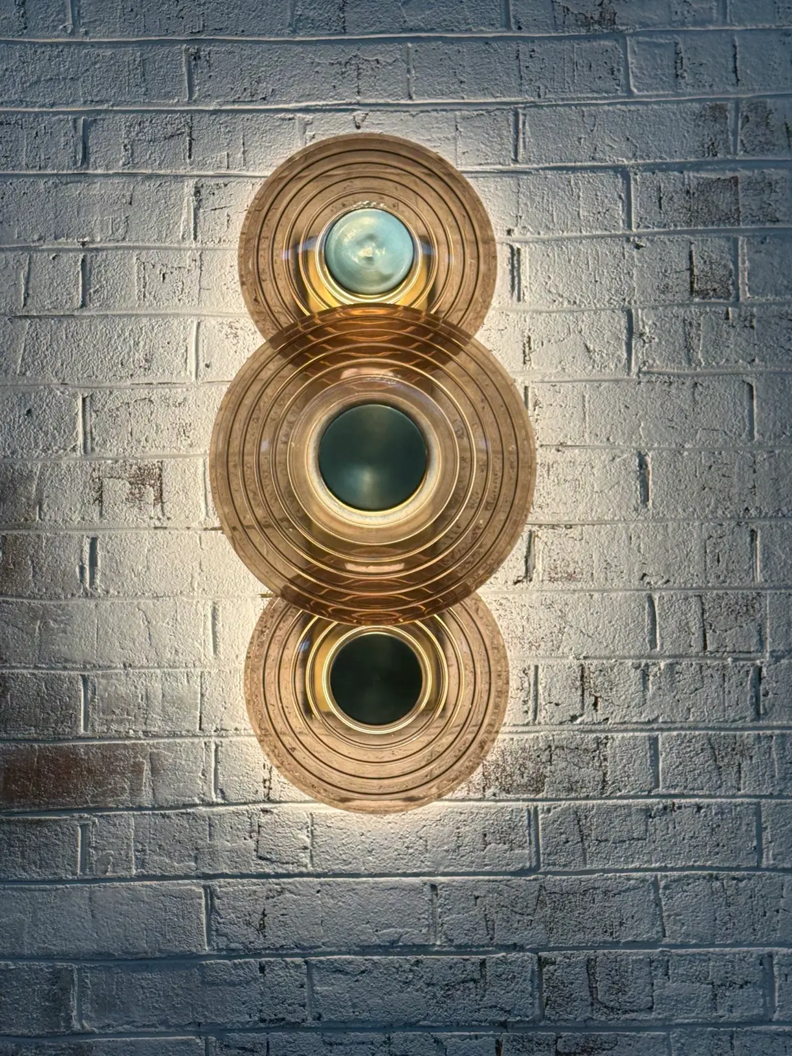 Decorative wall light with layered diffuser showing warm accent lighting on a brick wall