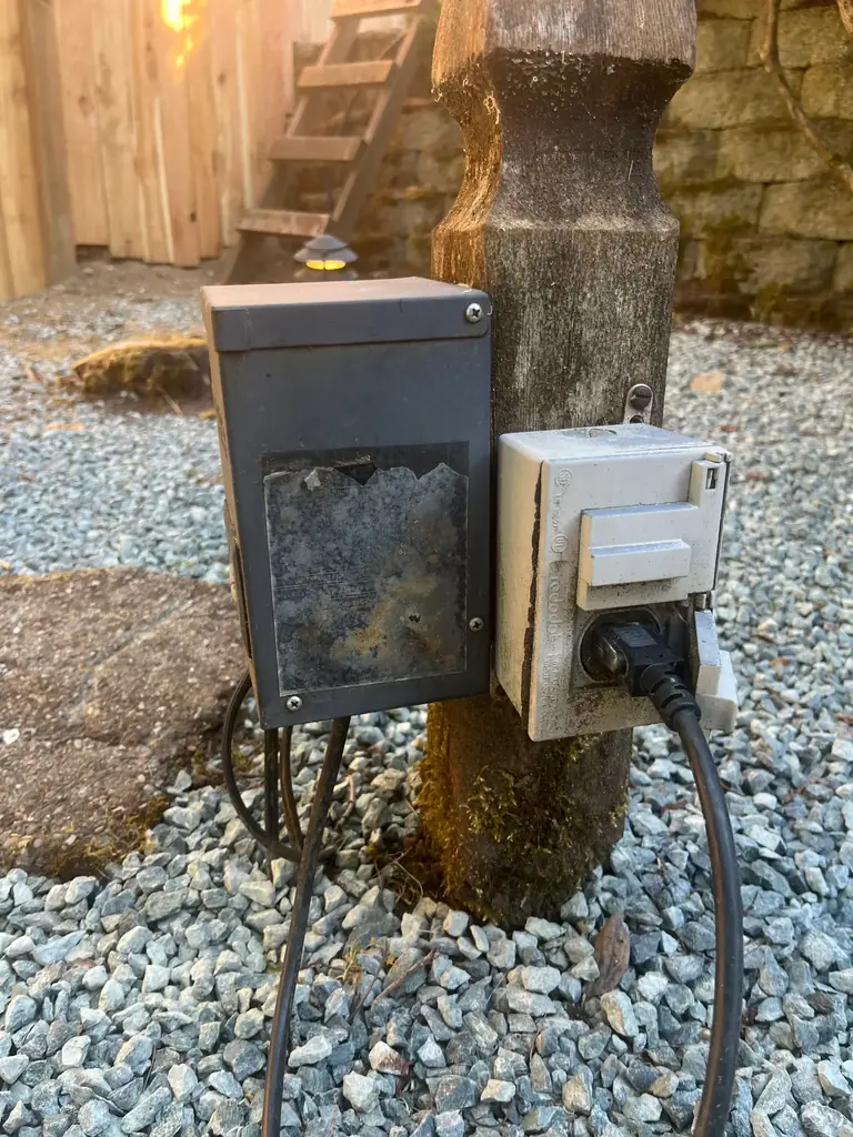 Aging Portfolio low-voltage landscape lighting transformer with corroded unreadable label and outdoor electrical receptacle
